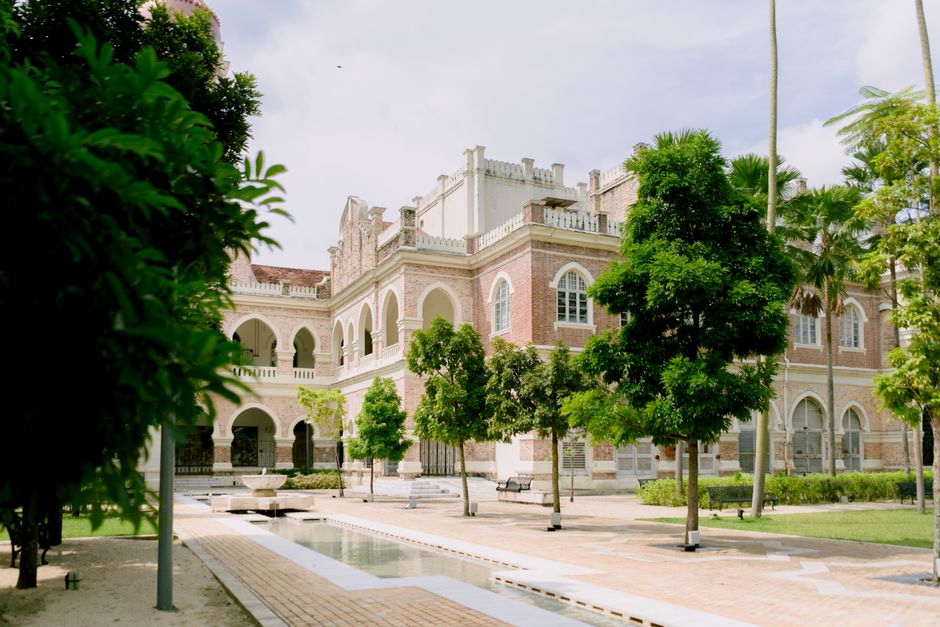 An arched colonial-era heritage building in Malaysia, ringed by a leafy courtyard.