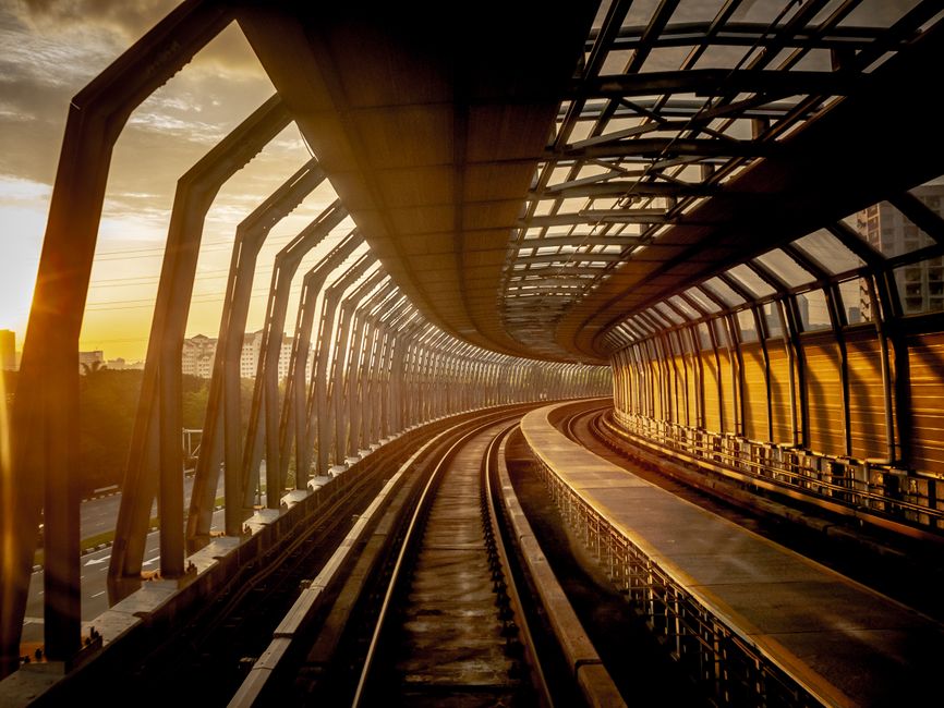 A Malaysian rail line curving toward the city at sunrise, the tracks glowing gold.