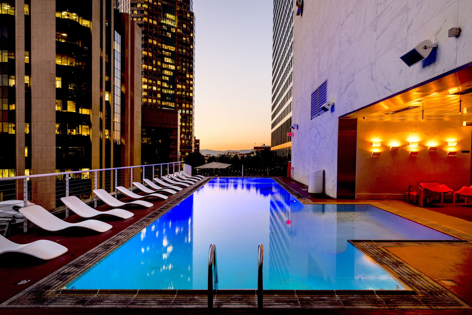 The outdoor pool lit warmly at dusk, with loungers lined up along the water's edge.
