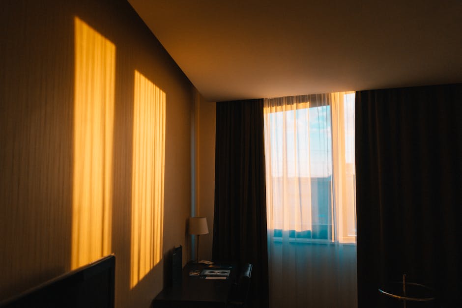 A calm double room at golden hour, with warm light falling through sheer curtains onto a window looking over the old town.